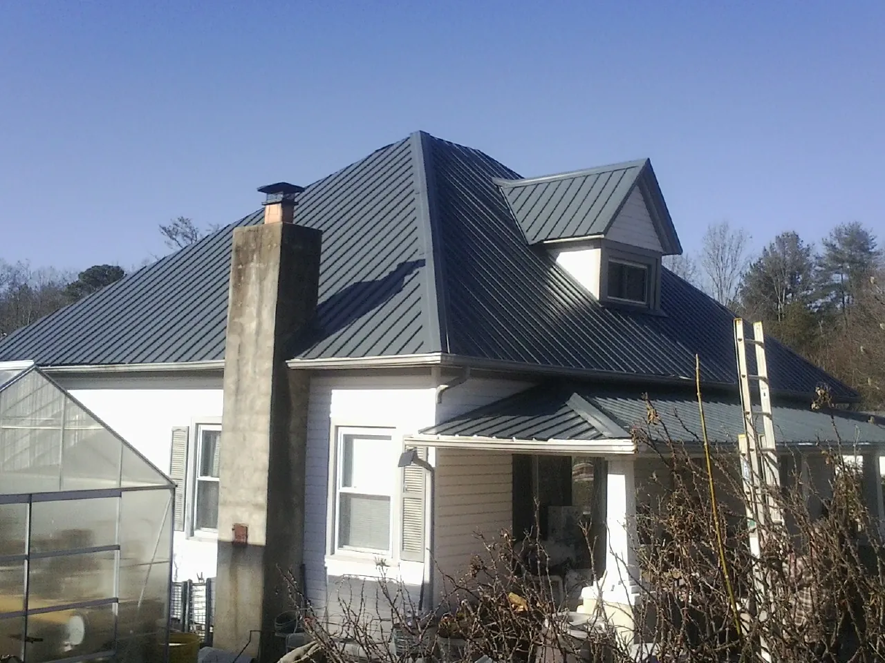 Dark blue standing seam metal roof on a white farmhouse with dormer — Slate & Tile Roof Repair by Roofing Brothers in Fort Howard