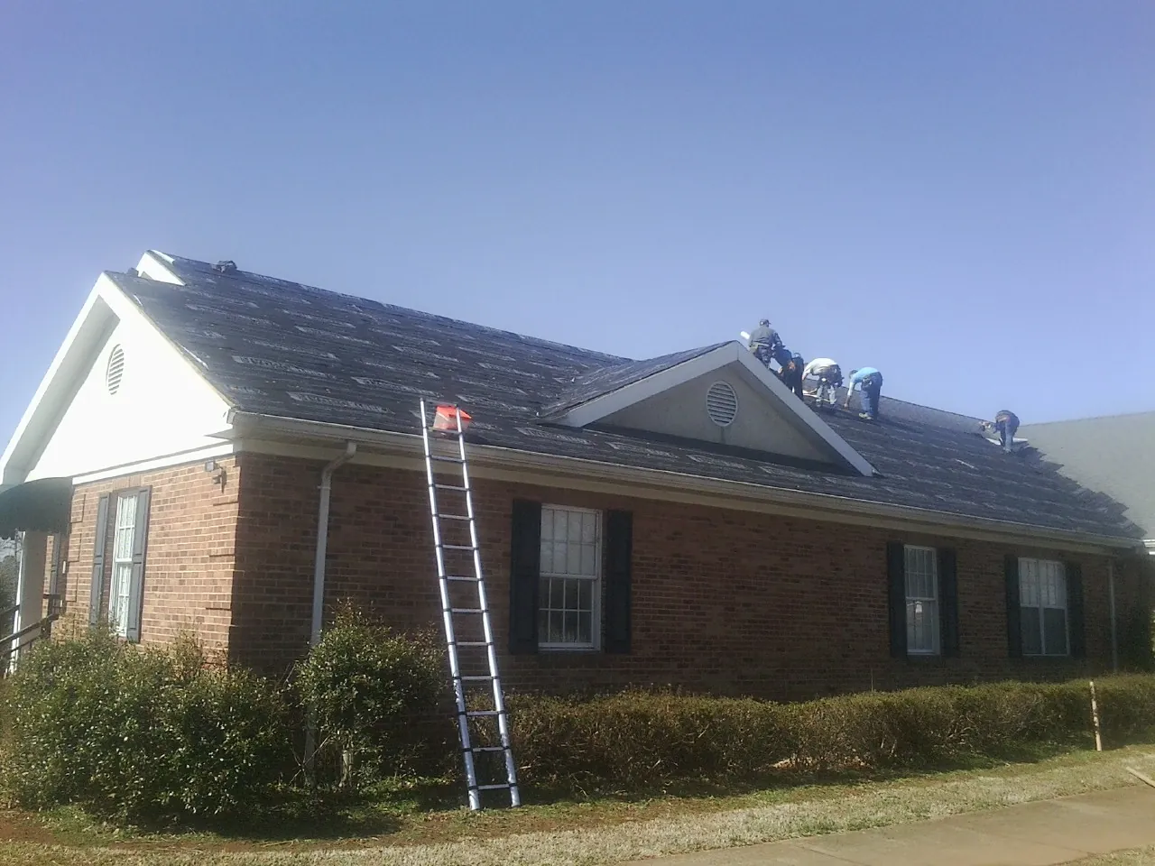 Crew tearing shingles off a brick ranch roof with a ladder set — Metal Roof Repair work by our crew in Fort Howard