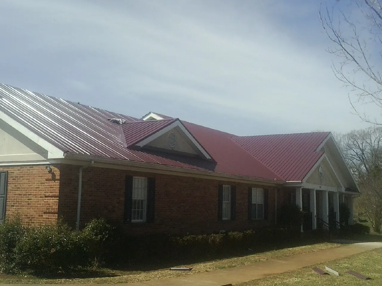 Red metal roof with gabled entries on a long brick building, from a Hail Damage Roof Repair job in Fort Howard