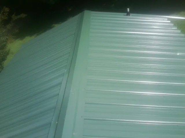 New green metal panels meeting at the ridge of a roof — Flat Roof Repair work by our crew in Fort Howard