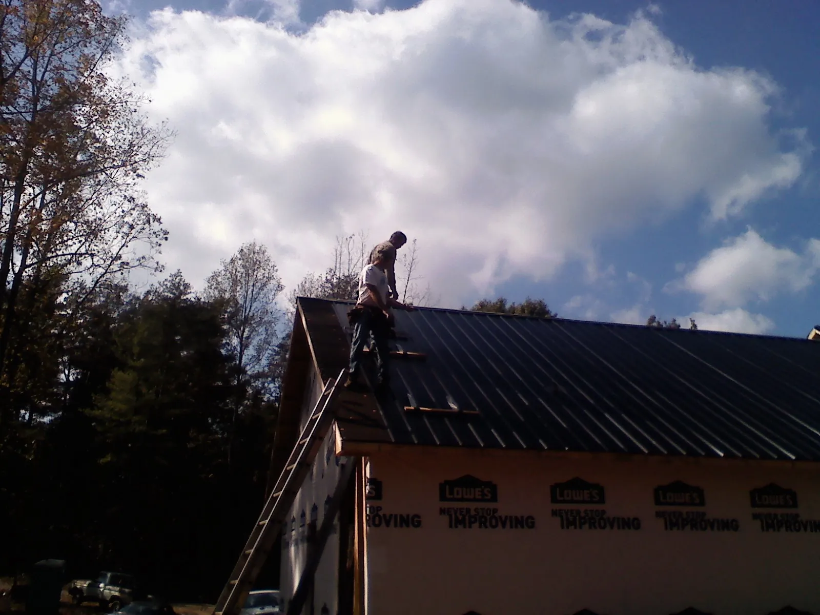 Roofer fastening dark metal panels high against a cloudy sky, from a Roof Inspection job in Fort Howard