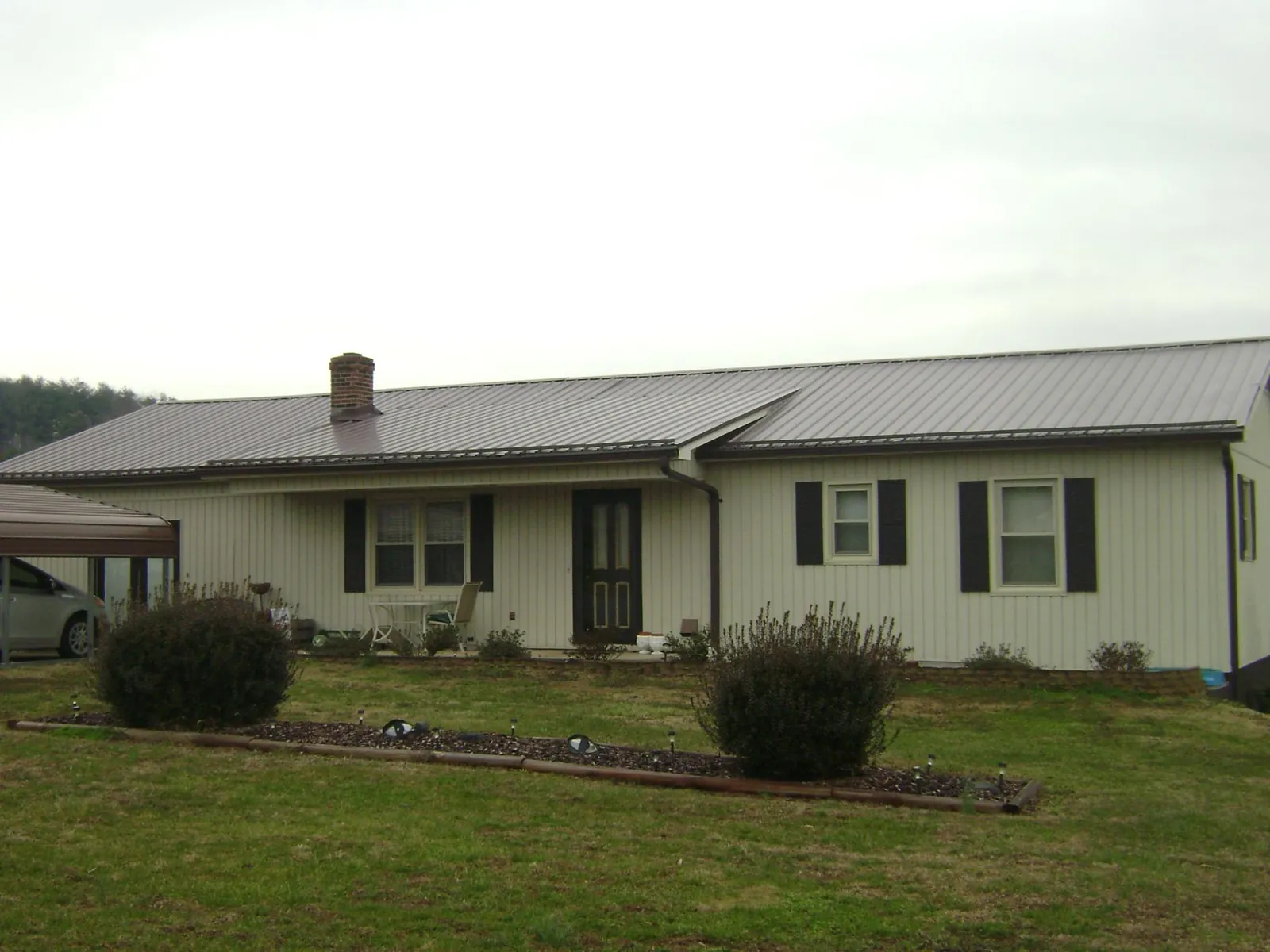 Brown metal roof on a cream sided ranch home with a brick chimney in Fort Howard