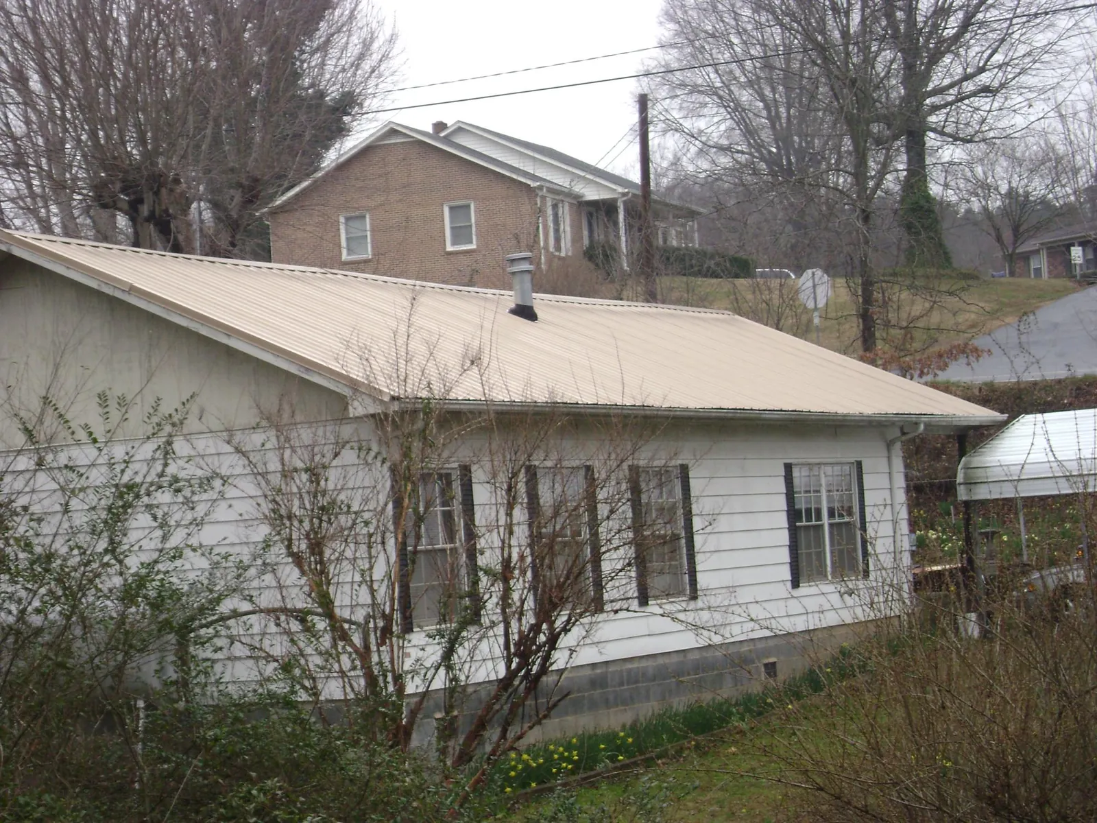 Tan metal roof on a white sided house set into a hillside — Commercial Roofing by Roofing Brothers in Fort Howard