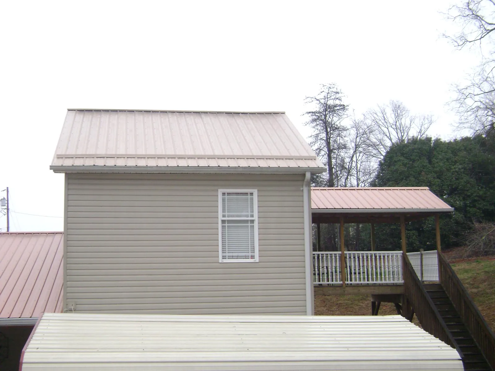 Tan metal roofs on a two story addition and attached porch, from a Roof Replacement job in Fort Howard